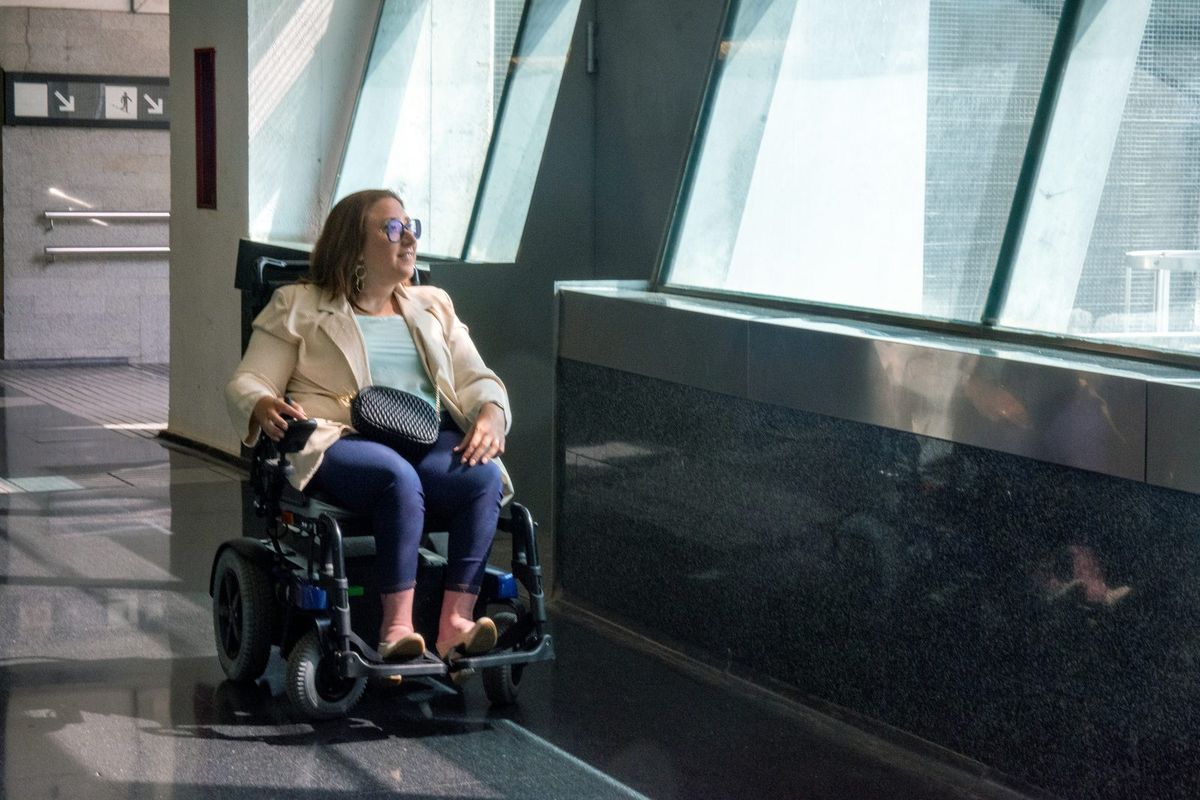 A woman in a power wheelchair moves through a bright office lobby.